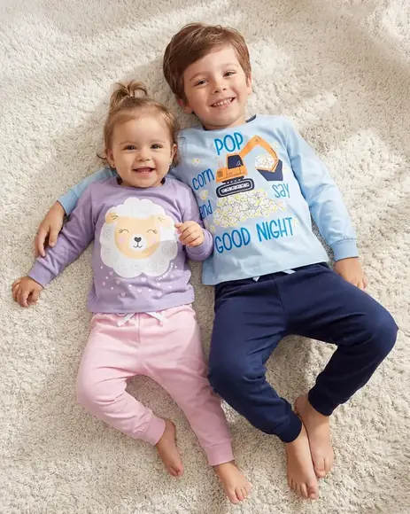Duas crianças de pijama deitadas sobre um tapete claro