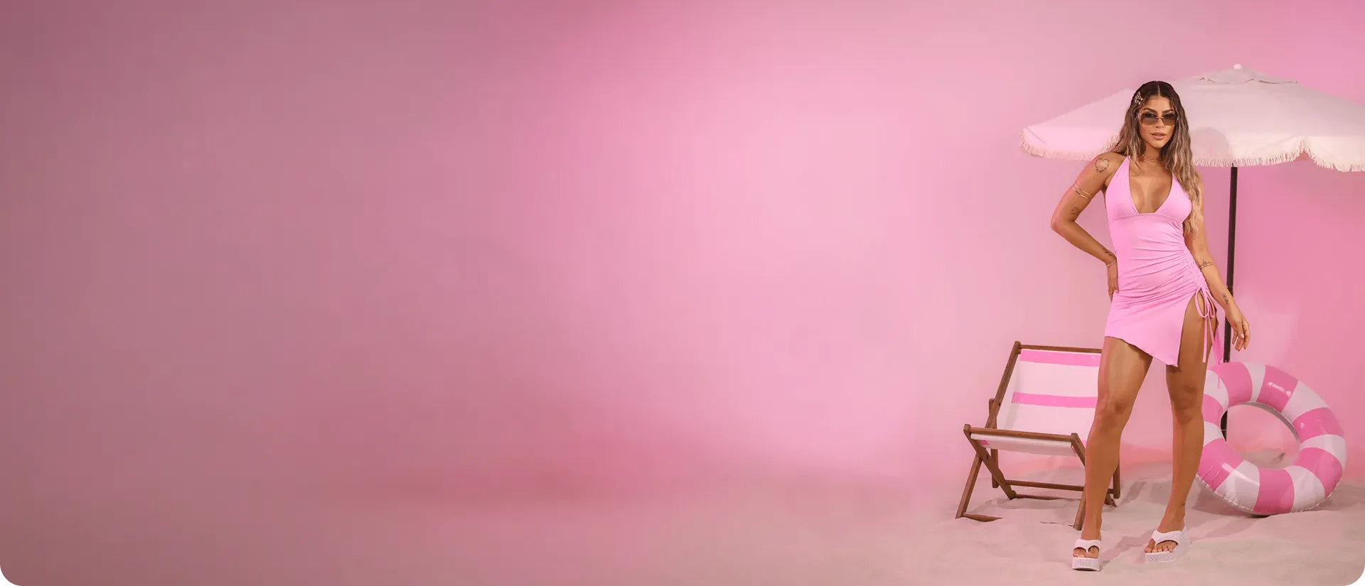 Modelo em ensaio de moda da Záfira, em cenário rosa com guarda-sol e cadeira de praia
